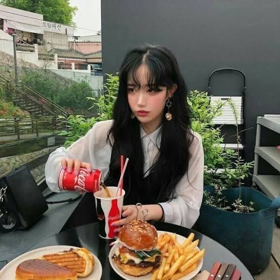 A woman sitting alone at an outdoor café table with a burger and fries