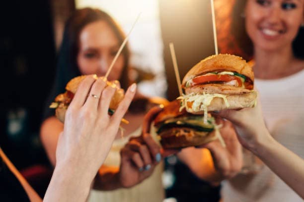 Friends raising burgers together across a table like a toast