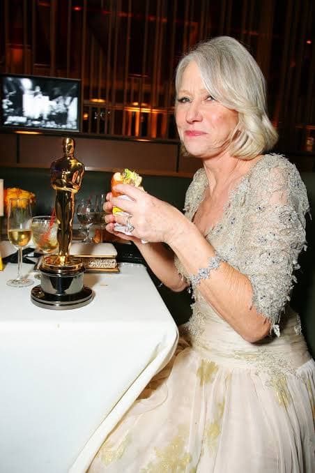 A woman in an evening gown eating a burger beside a gold statuette