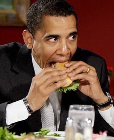 A man in a suit taking a bite of a burger at lunch